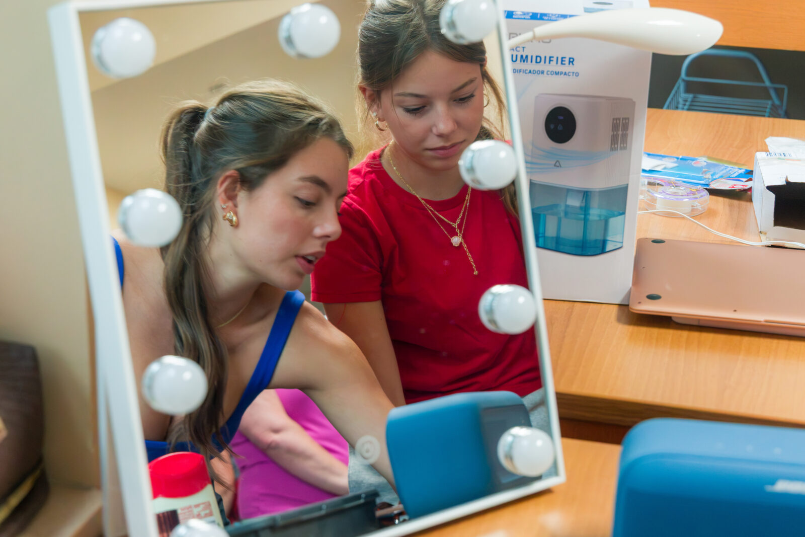 Two people reflected in a makeup mirror on a desk while unpacking