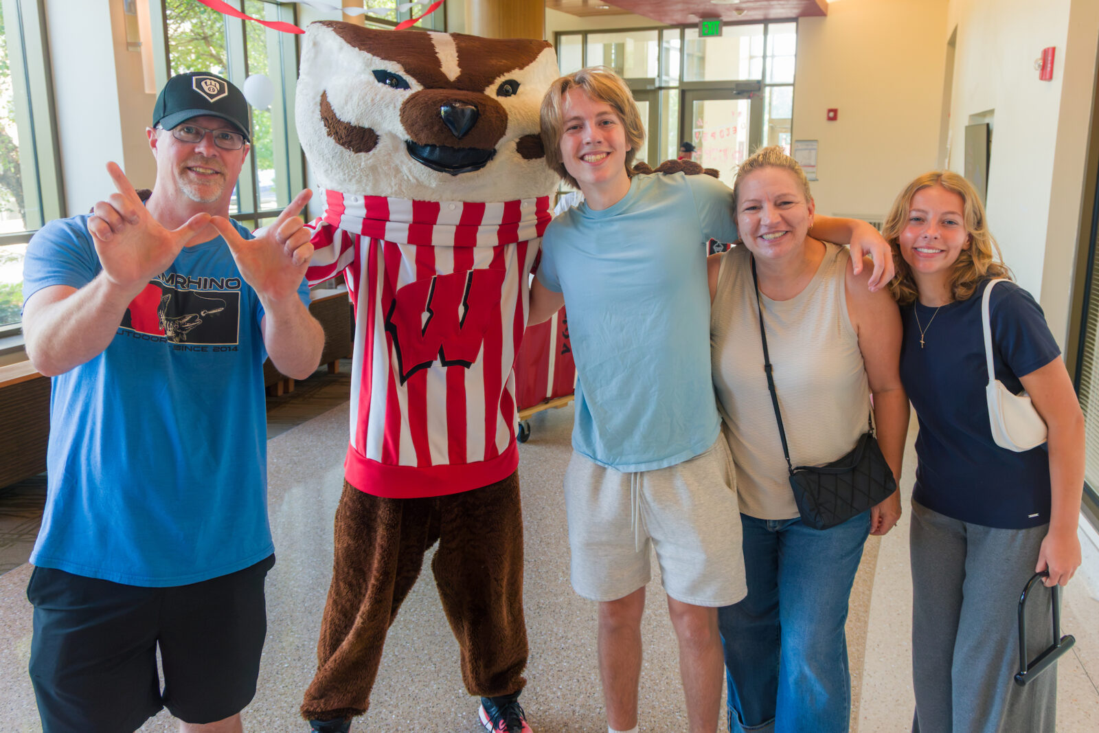 Bucky Badger poses with four people with one making the letter "W" with their hands