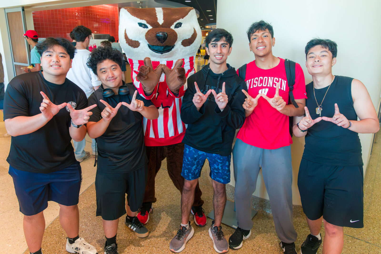Bucky Badger poses with a group of five people while they all make the letter "W" with their hands