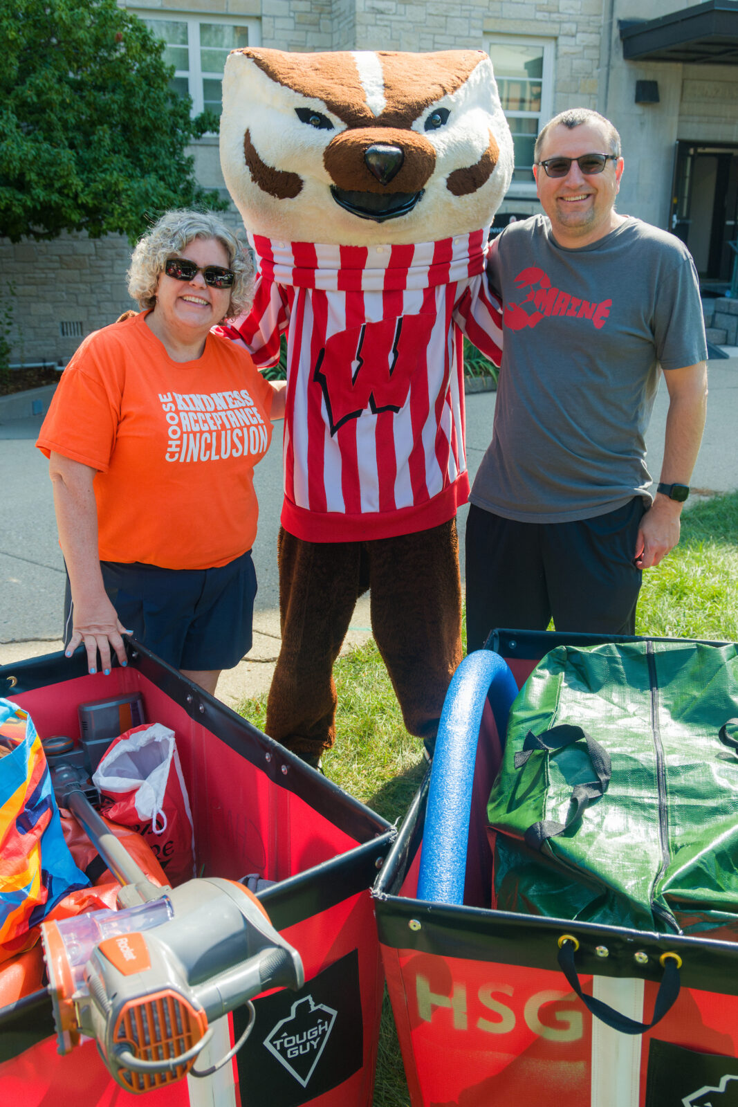 Bucky Badger poses behind red moving carts with two parents