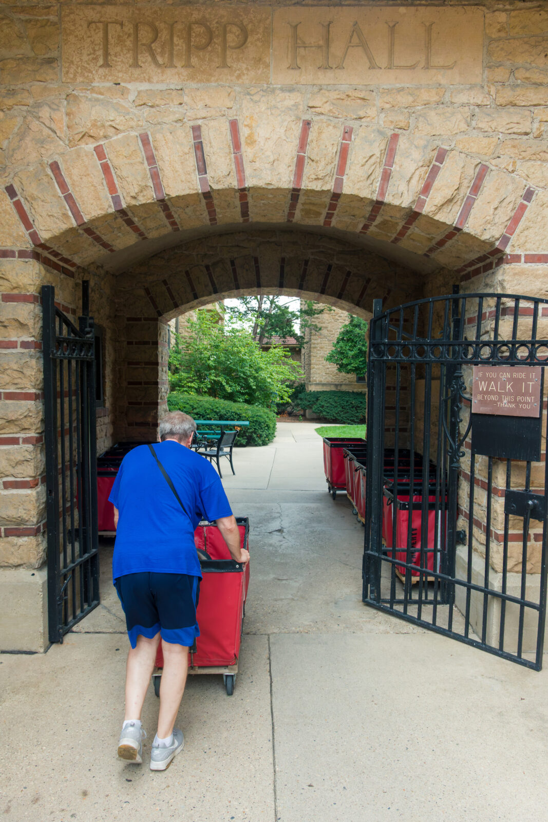 A person pushing a red moving cart through the archway with the words "Tripp Hall" on top