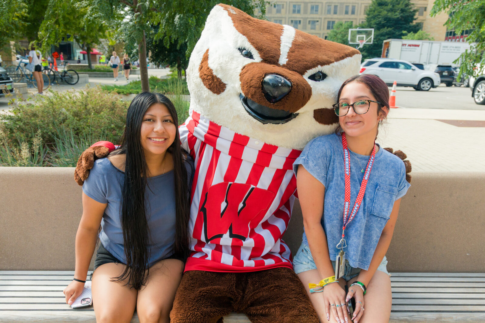 Bucky Badger and two people pose while sitting on a bench