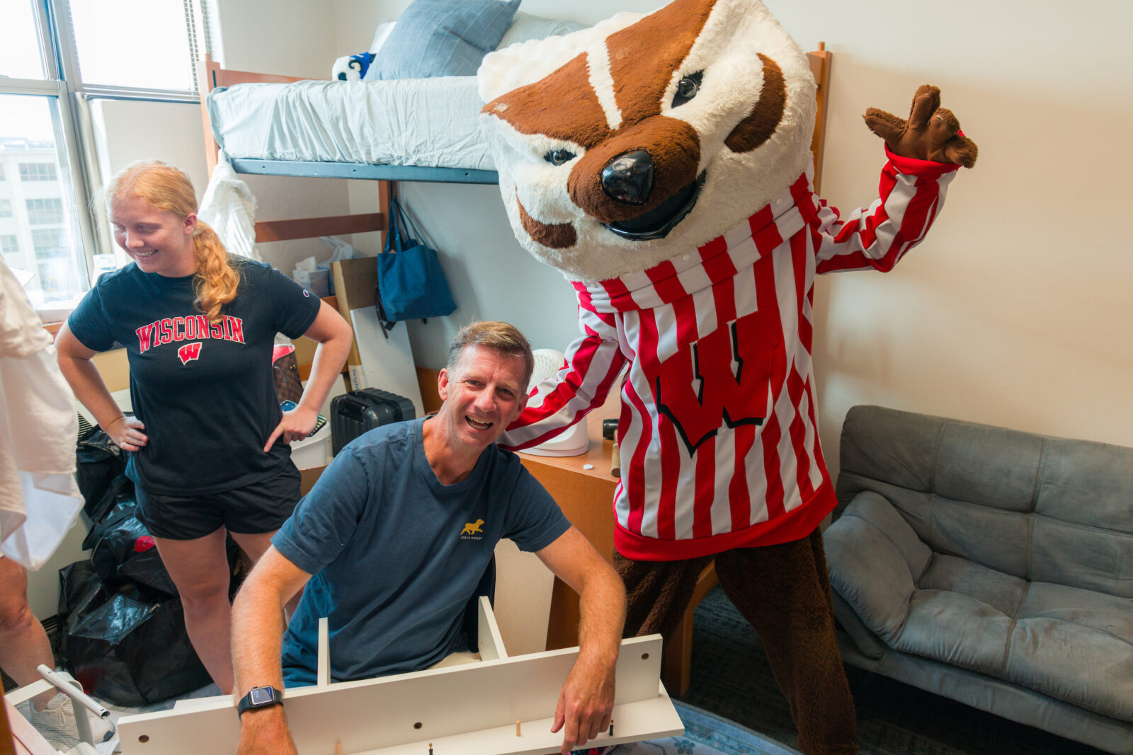 Bucky Badger and a Dad pose while putting together a bookshelf