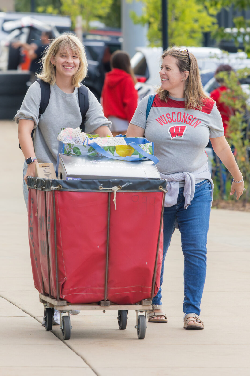 Two people smile while pushing a red moving cart