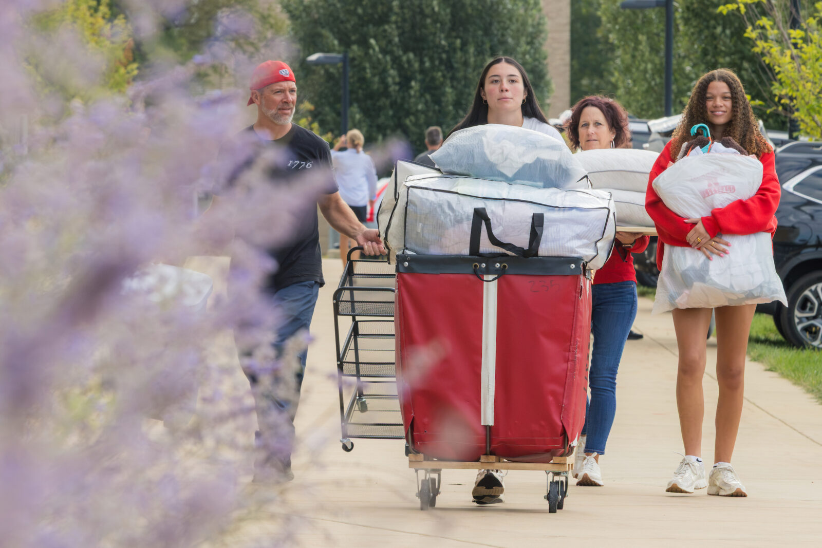Four people walking behind a red moving cart