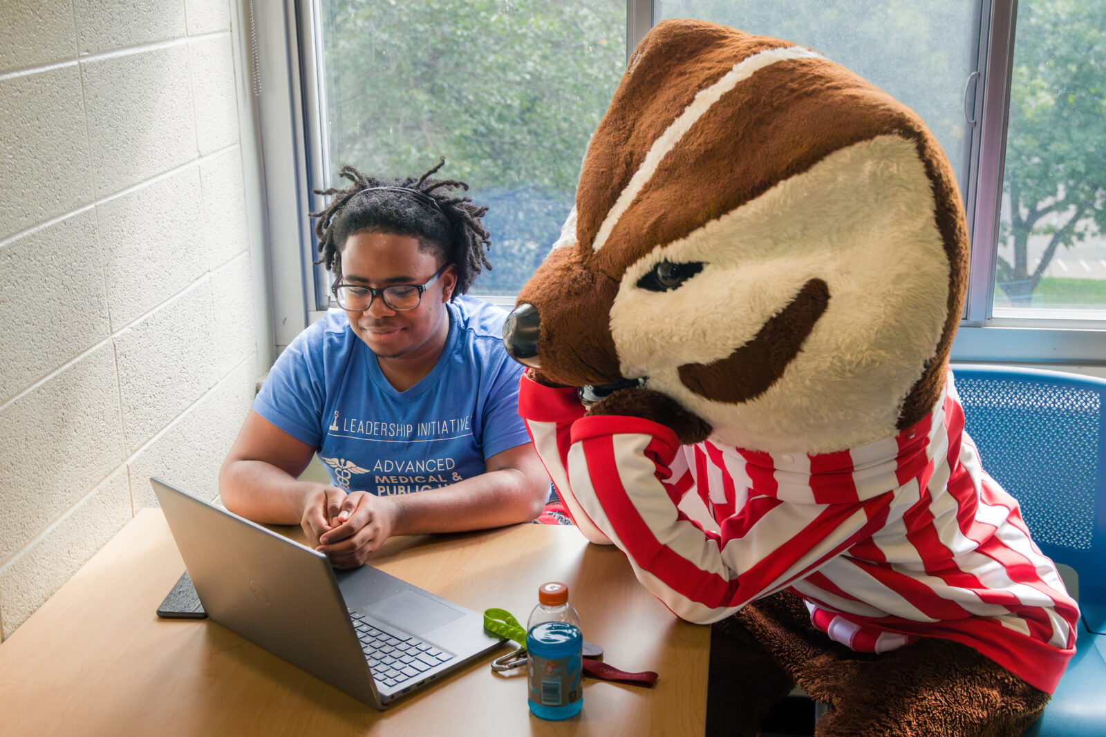 Bucky Badger and a student sitting at a table while looking at a laptop