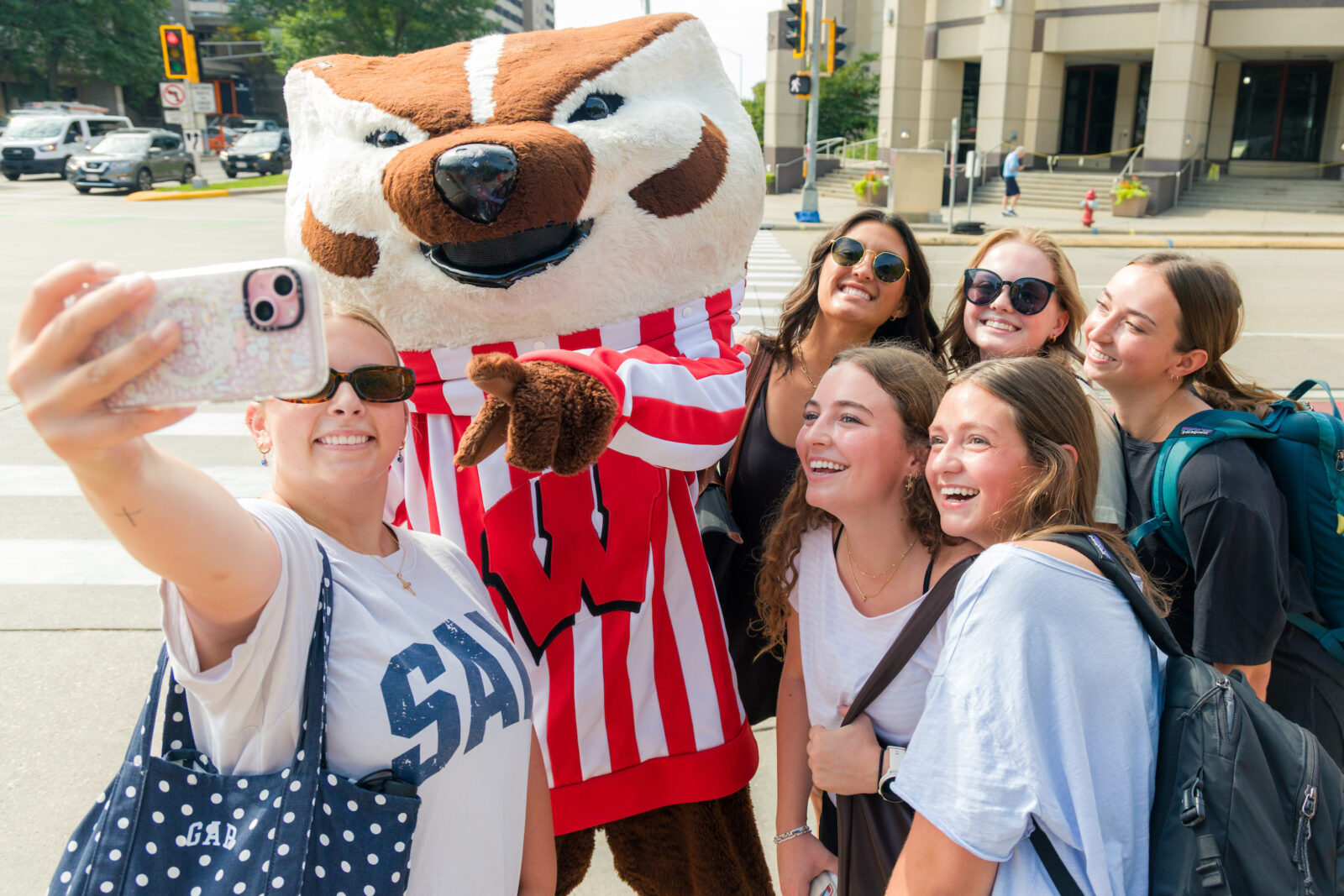 A group of six people take a selfie with Bucky Badger while he points at the phone