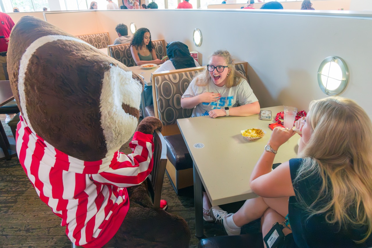 Bucky surprising two students at a table in Four Lakes during Badger Welcome Dinner