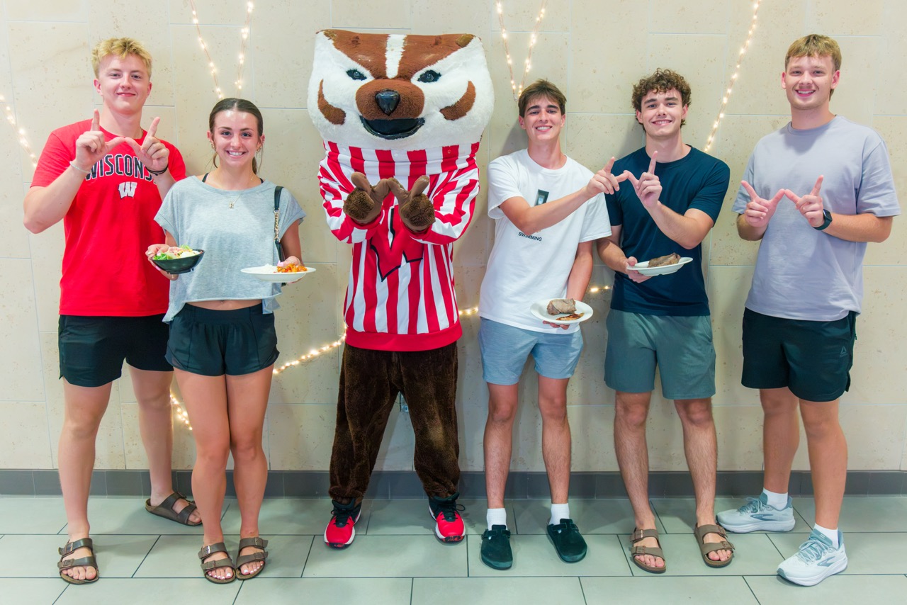 Bucky poses for photo with five students at the Badger Welcome Dinner