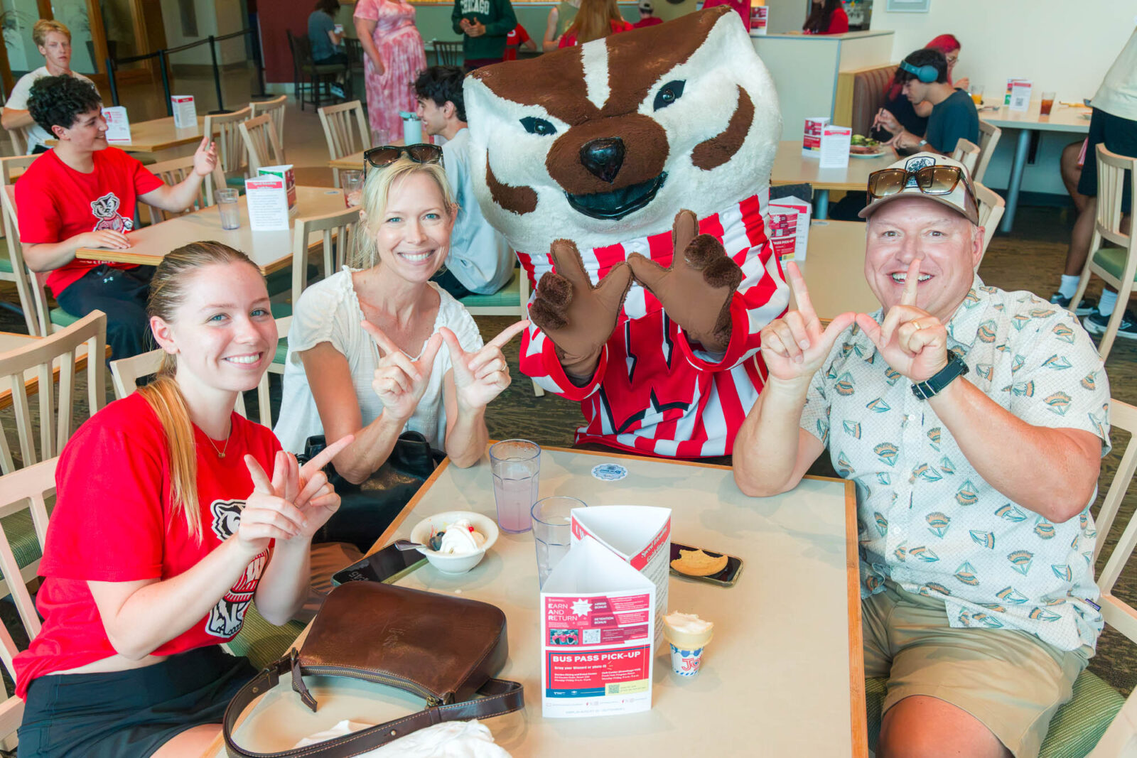 Bucky poses with a resident, mother, and father at a table in the Four Lakes Dining Room