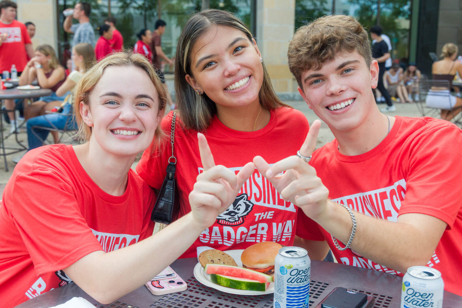 Three people smile for a photo at a table while two of the people make the letter "W" with their hands