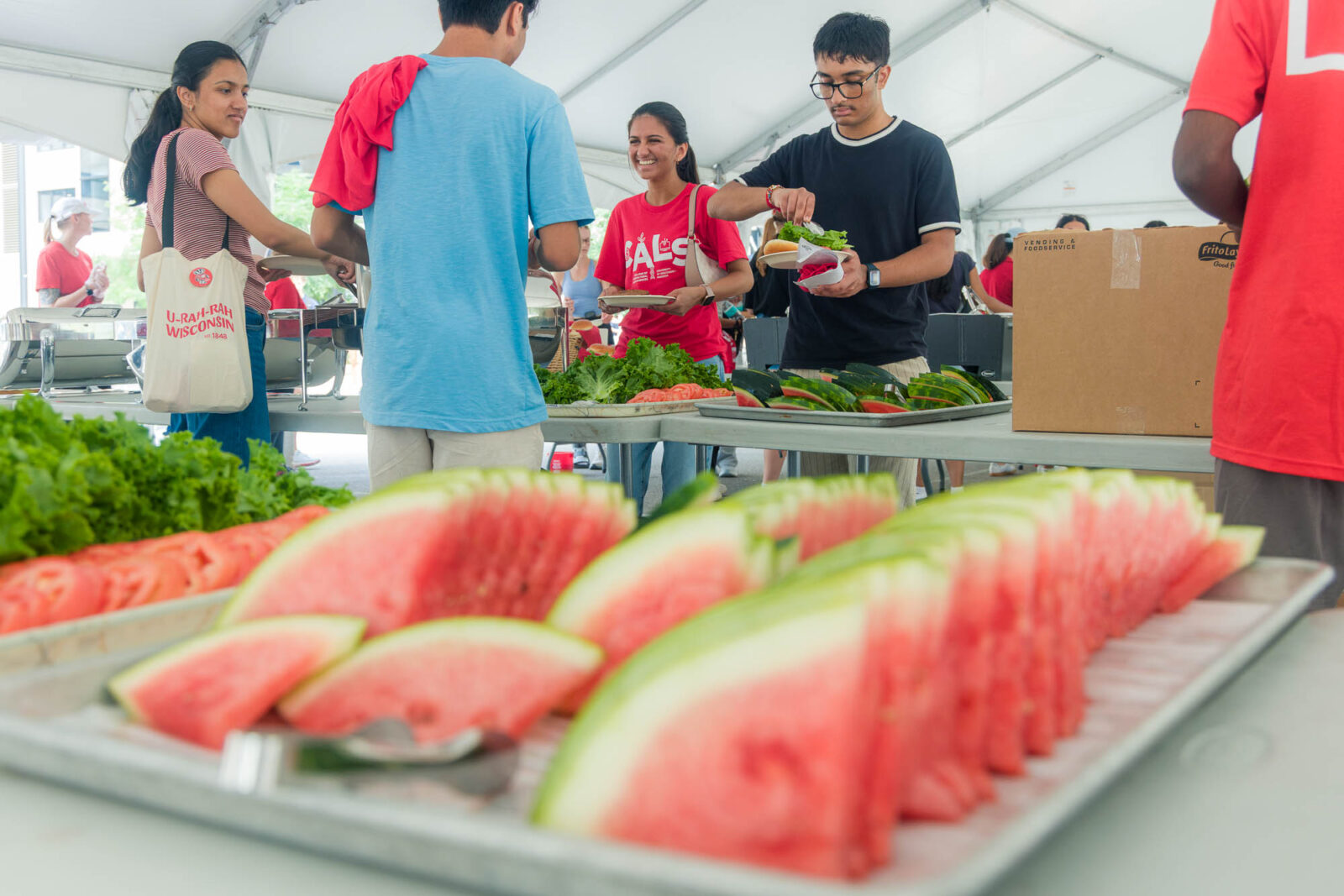 Watermelons are pictured in the foreground while students put food on plates in the background