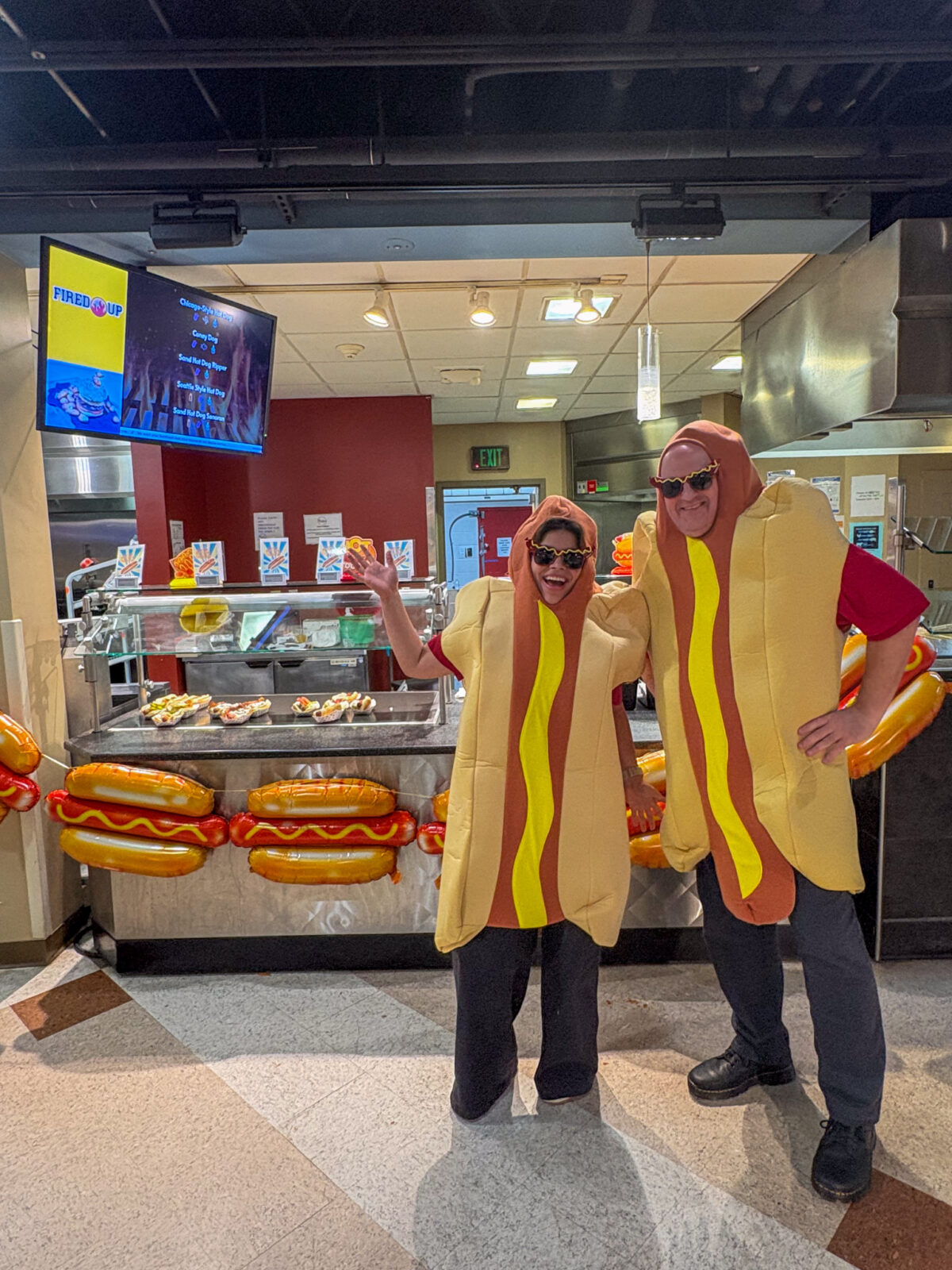 Staff dressed up in hot dog costume pose for photo by decorated hot dog station