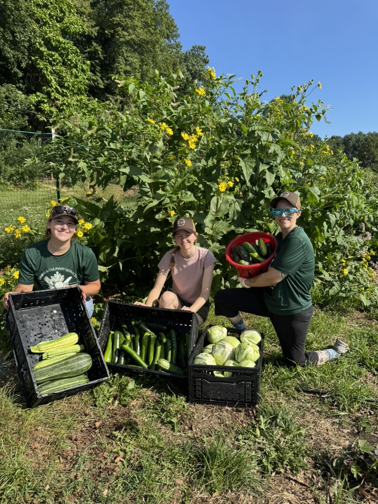 Staff pose for photo at the Campus Farm with vegetables from the day
